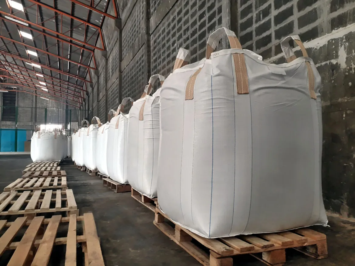 Fileira de big bags de ráfia em paletes de madeira num galpão industrial